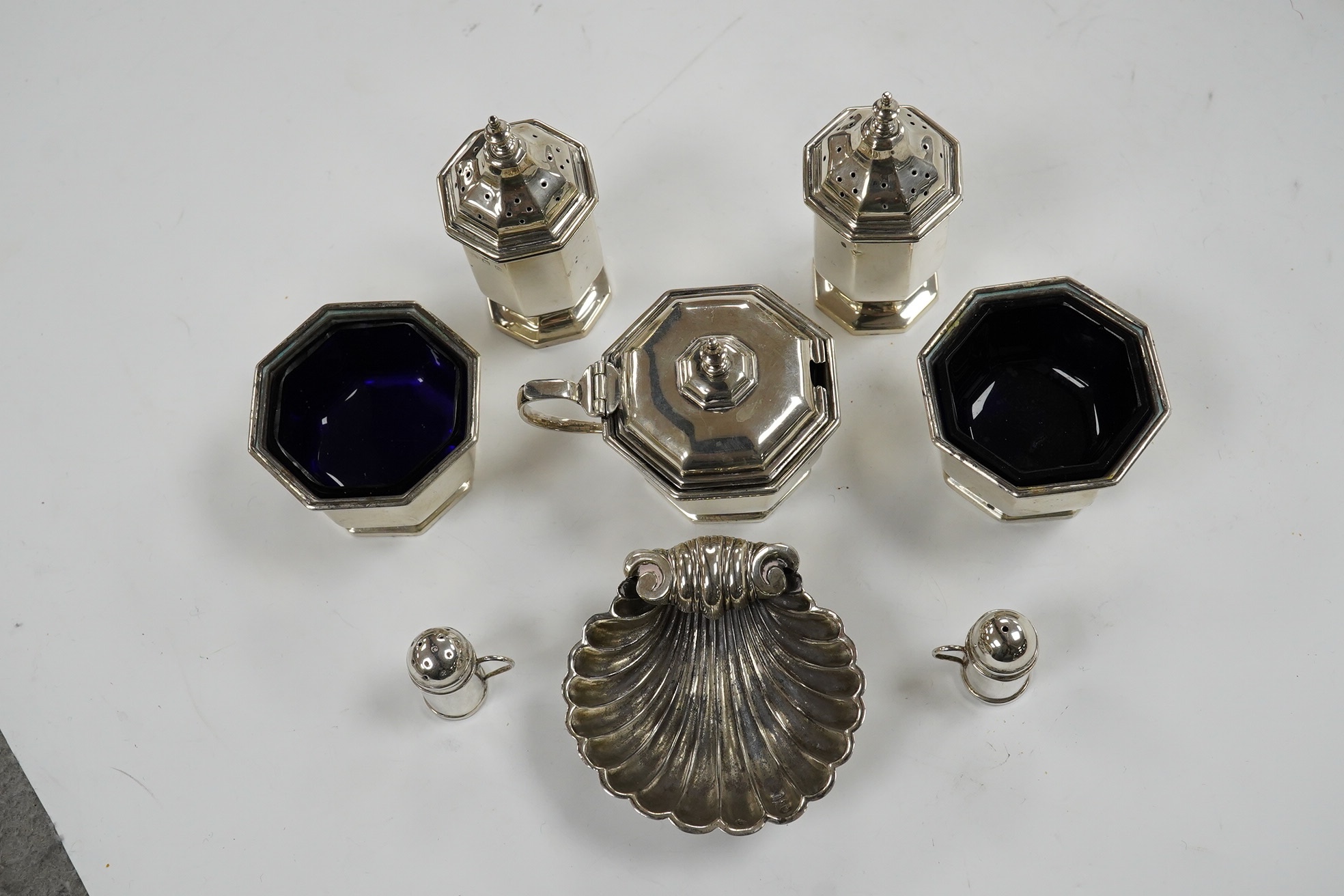 A George V five piece silver condiment set, Birmingham, 1931, two miniature 925 pepperettes and a silver shell salt. Condition - fair